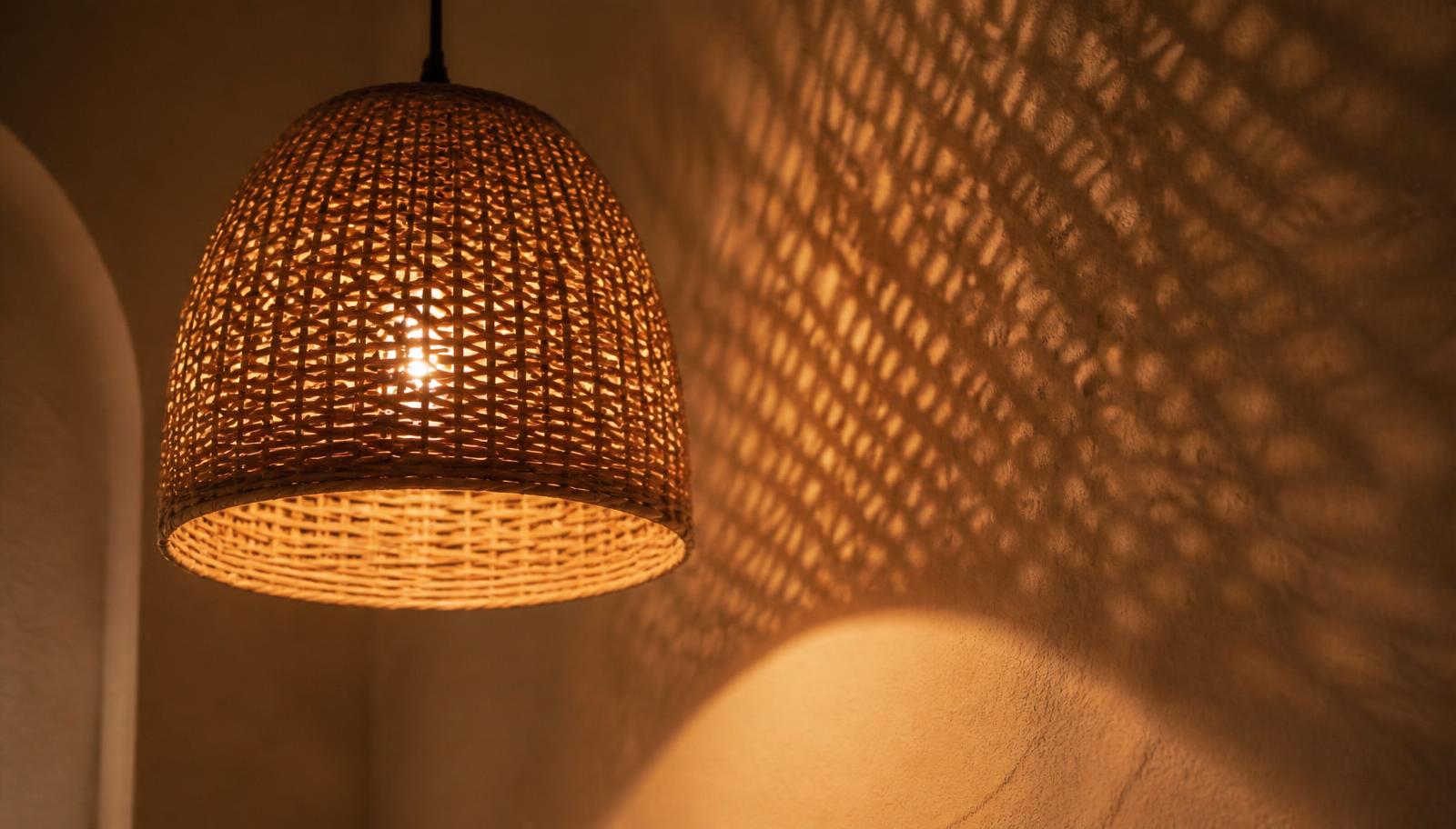 A handwoven rattan lampshade casting patterned shadow across a plaster wall
